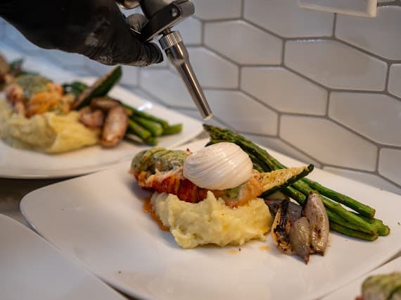 Stuffed lobster with accompaniments being finished with a torch