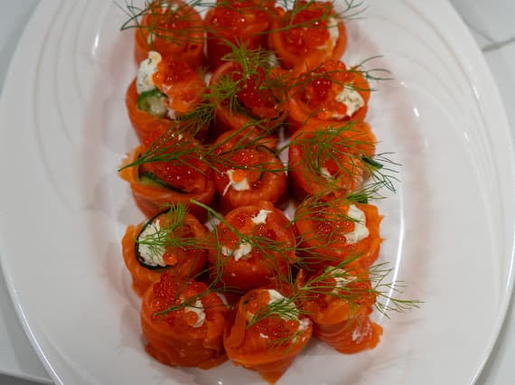Smoked salmon rolls topped with garnish on a white platter